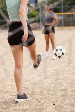 Güneşli bir plaj voleybol sahasında antrenman yapan iki sporcu, bir açık hava maçı sırasında takım çalışması ve atletizmi vurguluyor..