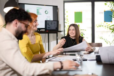 Profesyoneller bir iş toplantısında proje detaylarını tartışıyor ve ekrandaki çizelgeleri gözden geçiriyorlar. Atmosfer işbirlikçi ve odaklanmış, parlak bir ofiste takım çalışması sergiliyor..