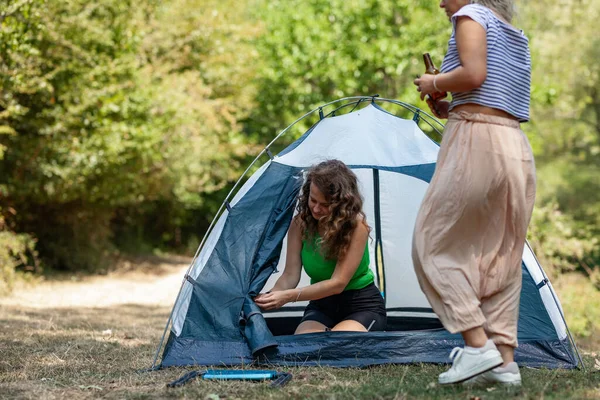 İki kadın ormanda kamp yapıyor. Biri çadırın içinde, diğeri dışarıda durup gülerek içkileri hazırlarken. Güneş ağaçların arasından parlıyor, sahneye sıcak bir his katıyor..