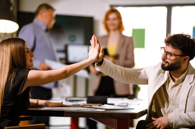 Ekip üyeleri parlak bir ofis alanında işbirliği yapıyor, fikirlerini paylaşıyor ve projelerinin ilerlemesini kutlamak ve ekip çalışması ve iletişimi geliştirmek için birbirlerine beşlik çakıyorlar..