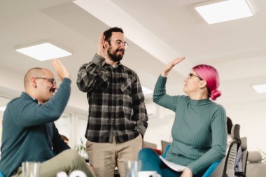 Parlak bir ofiste hevesle sohbet eden üç profesyonel. Gözlüklü bir adam ayakta dururken, iki oturan meslektaşı üretken bir takım tartışması sırasında fikirlerini paylaşarak jestlerle karşılık veriyor..