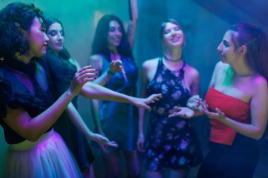 Bir grup arkadaş renkli ışıklarla çevrili bir partide eğleniyorlar. Kahkaha, sohbet ve dans havayı dolduruyor, neşe ve beraberliği canlı bir ortamda yakalıyor..