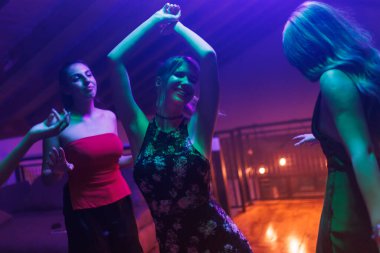 Canlı bir parti sırasında dans eden ve eğlenen bir grup genç kadın renkli, canlı ışıklandırmayla aydınlanan, neşeli anları kutlayan ve sosyal toplantıların enerji ve heyecanını sergileyen.