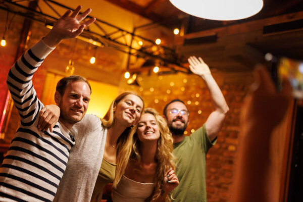 Four friends pose cheerfully indoors, enjoying quality time together under warm lighting, portraying happiness and friendship in a cozy, festive atmosphere with exposed brick walls