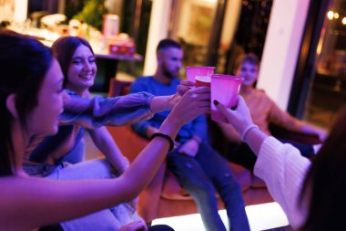 Dostlar neşeli bir anın tadını çıkarırlar. Renkli ve çağdaş bir iç mekanın içinde kadeh kaldırarak kadeh kaldırırlar. Canlı ve rahat bir atmosfer dostluğu ve kutlamaları vurguluyor..