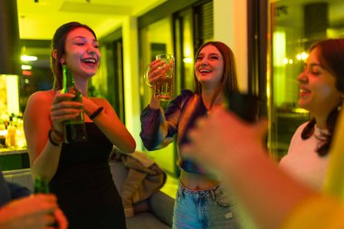 Bir grup genç arkadaş kapalı bir yerde toplanıp neşeli bir şekilde neşeli bir atmosferde içkilerle birlikte kahkahaların, yoldaşlığın ve mutluluğun ve pozitif enerjinin tadını çıkarıyorlar..