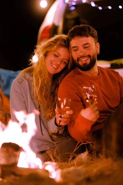 Bir çift, gece gökyüzünün altında bir kamp ateşinin yanında oturmuş ellerinde kadehlerle gülümsüyor ve kadeh kaldırıyorlardı. Etrafları yumuşak ışıklar ve sakin bir ortam ile çevrili. Sıcak bir ortam yaratıyorlar..