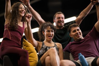 Dört arkadaş spor salonunda bir araya gelip fitness dersini tamamladıktan sonra bir kutlama anının tadını çıkarıyorlar. Gülümsüyor ve tezahürat yapıyorlar, neşe ve enerji paylaşıyorlar..