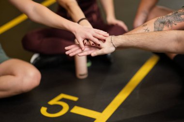 İnsanlar jimnastik salonunda toplanıp ellerini birleştiriyor. Spor salonunda destek veriyorlar. Çalışmalarla uğraşırken işbirliği ve cesaretlendirmeye odaklanırlar..