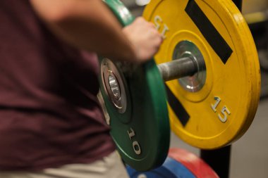 Spor salonundaki halterlere ağırlık plakası ekleniyor. Tabaklar farklı renk ve boyutlarda, ağırlıkları gösteriyor. Bu sahne kaldırma hazırlıklarını gösteriyor.