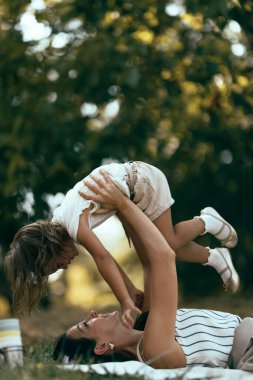 Güneşli bir günde anne ve çocuğun birlikte oynadığı iç açıcı bir sahne, doğal ortamda sevgi, neşe ve birlikteliği tasvir ediyor..