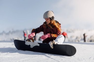 Snowboard yapmaya hazırlanan bir kız karda oturur. O bir kask takıyor ve gülümsüyor. Diğerleri kayak yaparken ve arka planda giderken. Bu sahnede dağlarda kış eğlencesi var..