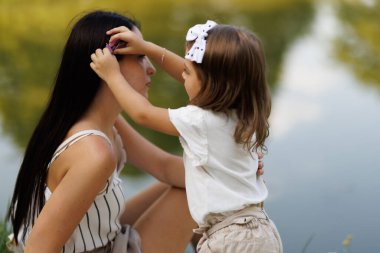 Şefkatli bir anne ve küçük kızı huzurlu bir gölün kenarında birlikte güzel bir günün tadını çıkarıyorlar. Ailevi yakınlık ve doğanın güzelliğini gösteriyorlar..