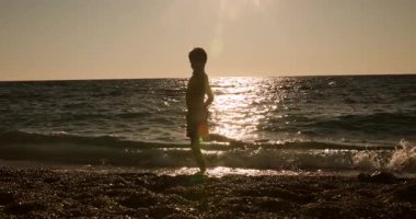 A Captivating Slow-Motion Shot of a Persons Silhouette Playfully Kicking and Splashing Golden Water at the Sun-Drenched Beach During a Beautiful Sunset, Creating Dynamic Water Spray.