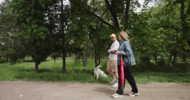 Bulutlu bir günde parkta köpeğini gezdiren bir çift. Ellerinde kahve ve şemsiye var..