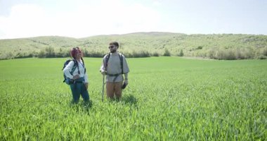 Sırt çantalı bir çift yürüyüşçü güneşli bir günde yeşil bir alanda manzaranın ve sohbetin tadını çıkarıyor..
