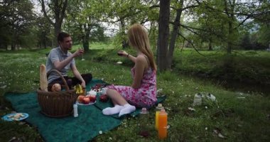 Genç bir çift nehir kenarındaki bir parkta romantik bir pikniğin tadını çıkarıyor. Yeşillik ve ağaçlarla çevrili yiyecek, içecek ve sohbet paylaşıyorlar..