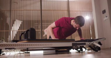 Şık bir spor salonunda, bir adam direniş eğitimi için tasarlanmış benzersiz fitness ekipmanlarını kullanarak zorlu bir antrenman rutinine girişir. Oturum boyunca odaklanması ve kararlılığı parlıyor..