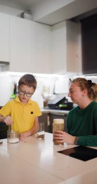 Genç bir çocuk ablası izlerken içkisine şeker ekler. Mutfak masalarında birlikte yemek tarifi hazırlıyorlar..
