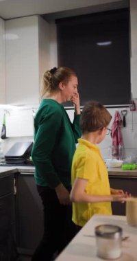 Bir anne ve oğul mutfaklarında birlikte yemek hazırlıyorlar. Malzeme ekliyorlar ve yemek yaparken birbirlerine sevgiyle bakıyorlar..