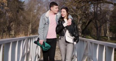 Birbirine aşık genç bir çift güneşli bir günde parktaki köprüde yürür. El ele tutuşup birbirlerine bakıyorlar..