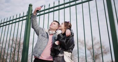 Genç bir çift selfie çeker ve parkta hassas bir anı paylaşır. Fotoğraflara bakıp gülümsüyorlar..