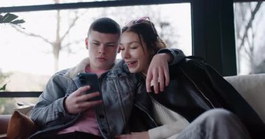 Genç bir çift birbirine yakın oturuyor ve akıllı telefona bakıyor. İnternette geziniyorlar ve tartışıyorlar..