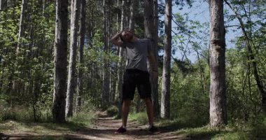 Bir insan, uzun ağaçlar ve doğa ile çevrili, parlak güneş ışığı altında bir orman yolunda duruyor. Sakin atmosfer, insanlarla açık hava arasındaki bağlantıyı vurguluyor..