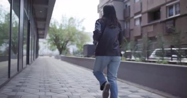 Genç bir kadın ağaçlarla kaplı bir şehir yolunda koşuyor, modern bir şehrin ortasında sağlıklı bir yaşam tarzı sergiliyor..