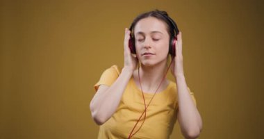 Huzurlu genç bir kadın kırmızı kulaklıkla müzik dinler, gözlerini kapatır ve parlak sarı bir arka plana hafifçe gülümser..