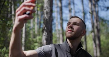 Genç bir adam, parlak güneş ışığı altında yemyeşil bir ormanda anları yakalar. Huzurlu bir ortamda yaşadığı deneyimi belgelemek için doğanın tadını çıkarıyor..