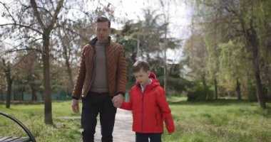 Bir baba ve oğlu yemyeşil bir parkta el ele geziyor. Hava açık ve güneşli. Birlikte güzel bir doğa deneyimi yaşayacağız..