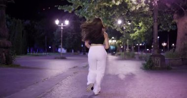 Genç Asyalı bir kadının gece parkta koşarken çekilmiş dinamik bir fotoğrafı. Saçları rüzgârda güzel bir şekilde savrulurken spor yaparken..