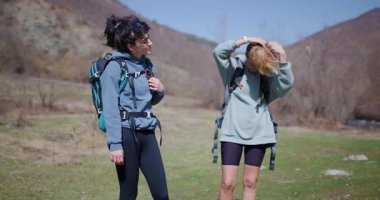 Yürüyüş yapan iki genç kadın mola verip saç düzeltiyor. Mutlular ve güneşli günün tadını çıkarıyorlar..