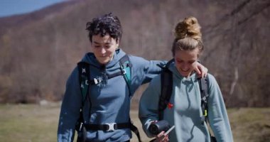 İki bayan arkadaş doğa yürüyüşü yapıyor. Telefonlarındaki fotoğraflara bakıyorlar ve birlikte geçirdikleri zamanın tadını çıkarıyorlar..