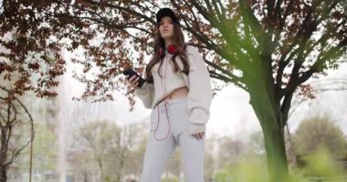 Parktaki Genç Kız, Elinde Cep Telefonu Tutarken Kulaklıkla Müzikten Hoşlanıyor