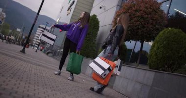 İki mutlu genç kız alışveriş merkezinin önünde durmuş alışveriş torbalarıyla konuşuyor ve başarılı alışveriş çılgınlıklarının tadını çıkarıyorlar..