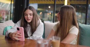 İki genç kız bir kafede oturuyor, telefona bakıyor ve tartışıyorlar. Gülümsüyorlar, gülüyorlar, birlikte eğleniyorlar..