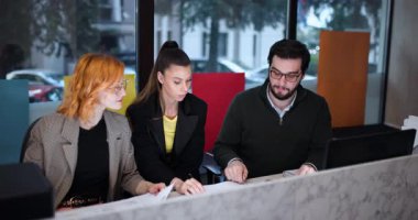 Üç kişilik bir grup bir ofis ortamında toplanıyor. Dizüstü bilgisayarlarda birlikte çalışıyorlar ve fikirlerini kağıt üzerinde paylaşıyorlar. Hafta içi sabahları görevlerine odaklanmış ve meşgul görünüyorlar..