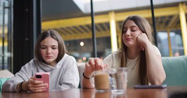 İki genç kız bir kafede oturup kahvelerini içip telefonlarına bakıyorlar. Biri içkisini karıştırıp yudumlarken, diğeri cep telefonunu karıştırıyor..