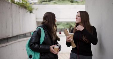 Okuldaki dersler arasında sohbet edip kahve içen iki genç kız.