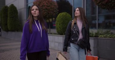 Alışveriş yaptıktan sonra sohbet eden iki mutlu genç kız. Alışveriş torbaları taşıyorlar ve neşeli ifadeleri var..