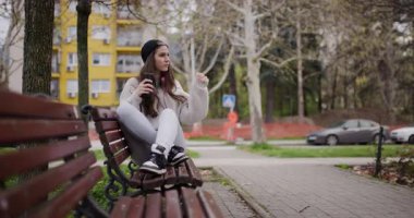 Genç kız, parkta otururken telefonunda müzik dinlemekten hoşlanıyor.