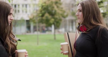 Kahve ve dizüstü bilgisayarla parkta sohbet eden iki genç kız: Modern Arkadaşlığa Bir Bakış