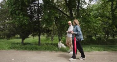 Bulutlu bir günde parkta köpeğini gezdiren bir çift. Ellerinde kahve ve şemsiye var..