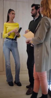 Öğleden sonra modern bir ofiste üç kişi buluşuyor. Proje fikirlerini tartışıyor, notlarını paylaşıyor ve ahşap bir duvarın yanında dururken fikir alışverişinde bulunuyorlar..