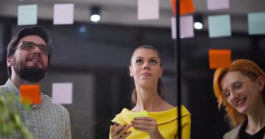 Gün boyunca üç kişi bir ofis ortamında toplanıyor. Fikirleri planlamak ve tartışmak için yapışkan notlar kullanıyorlar. Atmosfer odaklı ve işbirlikçi..