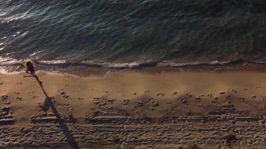 Gün batımında kumsalda koşan ve yürüyen bir kadın. Okyanus tarafından egzersiz yapan kadın koşucunun havadan görünüşü. Sağlık ve zindelik kavramı.