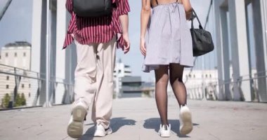 Gündelik yaz kıyafetleriyle köprüde yürüyüp şehir ortamında sırt çantalarıyla güneşli bir günün tadını çıkaran bir çiftin arka görüntüsü..