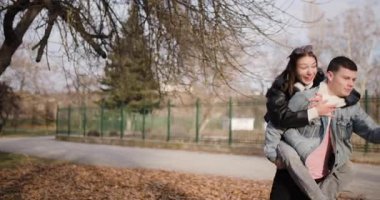 Genç bir adam, kız arkadaşını telefonla selfie çekerken parkta sırtında taşır. Eğlenirken gülümser ve gülerler..